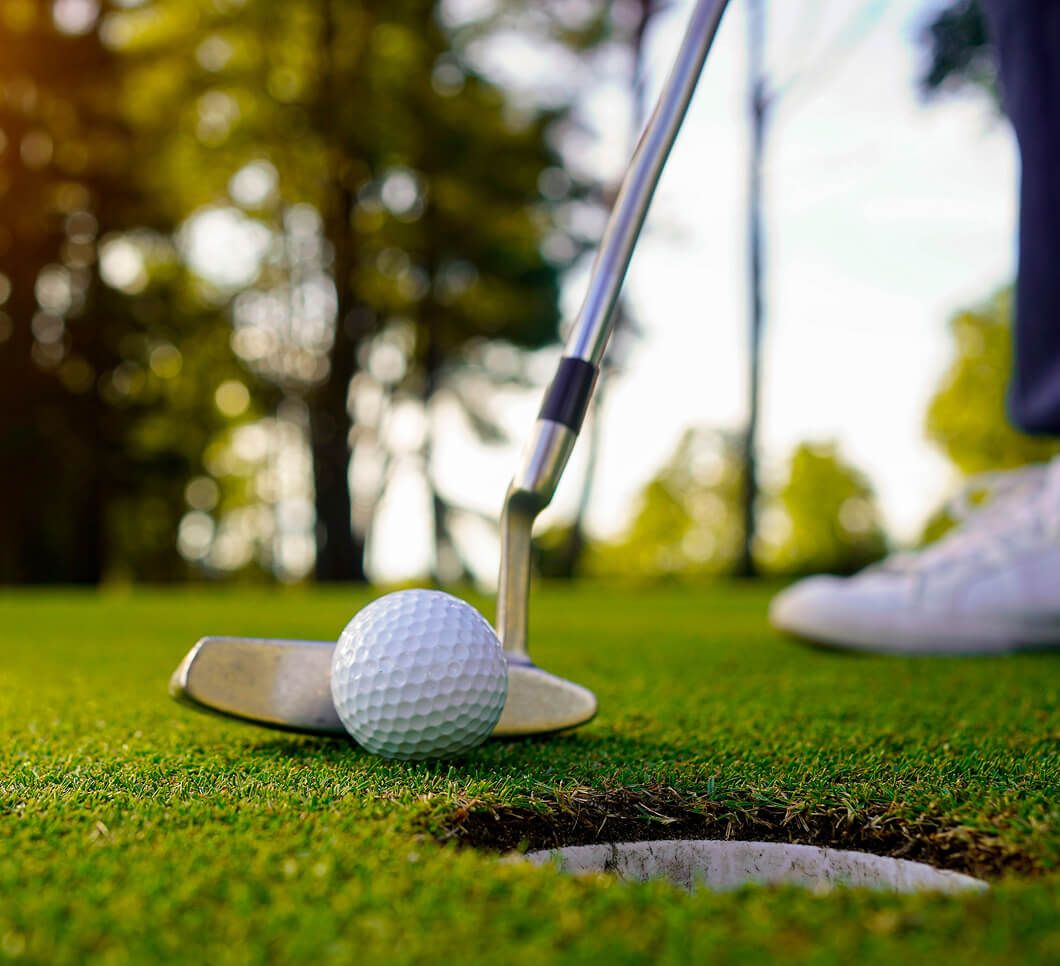 A golf club about to putt a ball into a nearby hole