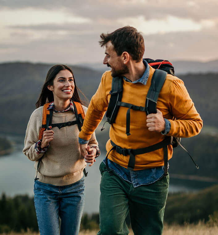 A man and woman are holding hands smiling at each other as they backpack up a mountain.