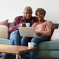 Elderly couple on couch review information together on a laptop while drinking tea