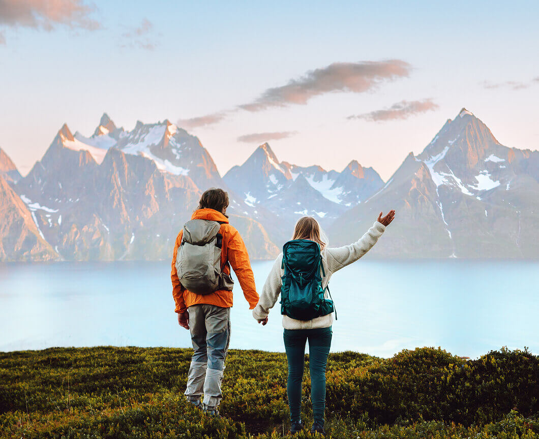 A hiking couple holding hands while looking at a mountain and lake