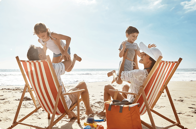  Family relaxing on the beach in striped deck chairs, with parents playing joyfully with their young children near the shoreline on a sunny day