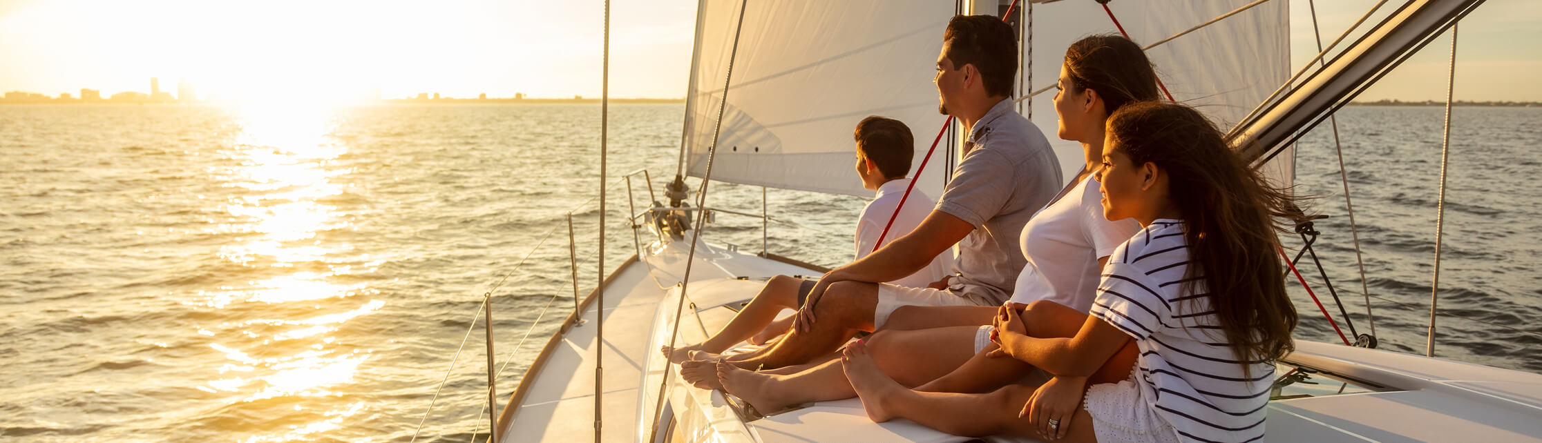 A family sitting on top of a boat looking offscreen at a sunset.