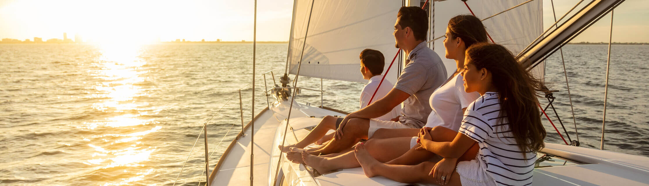 A family sitting on top of a boat looking offscreen at a sunset.