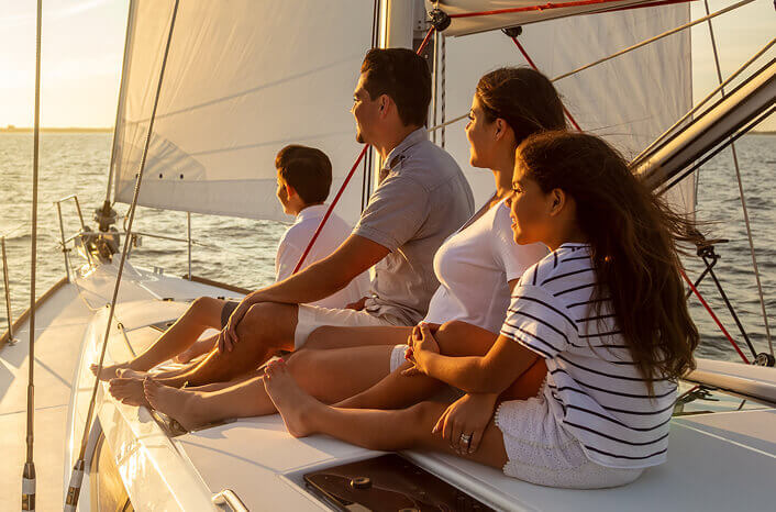 A family sitting on top of a boat looking offscreen at a sunset.