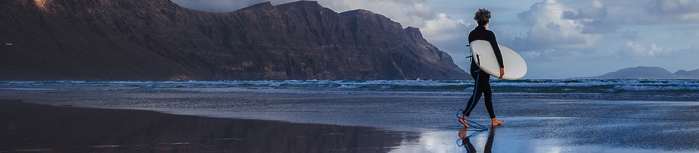 A surfer with a surfboard walking on the beach toward the ocean