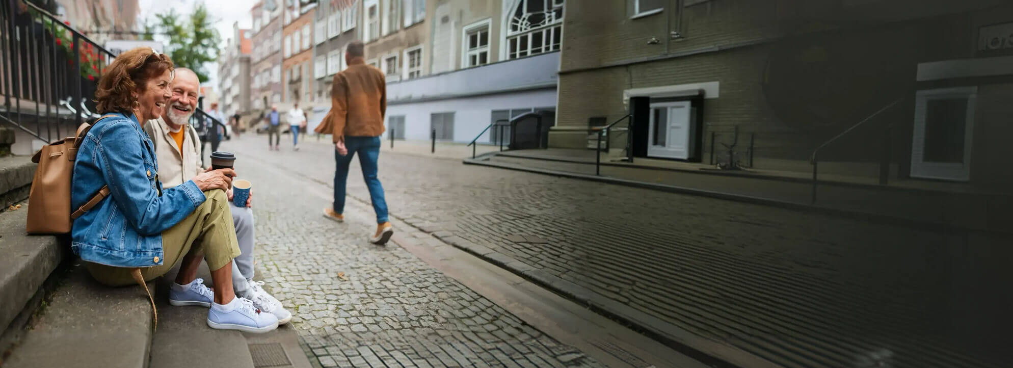 An older couple sitting on the steps of a building while holding coffee cups.