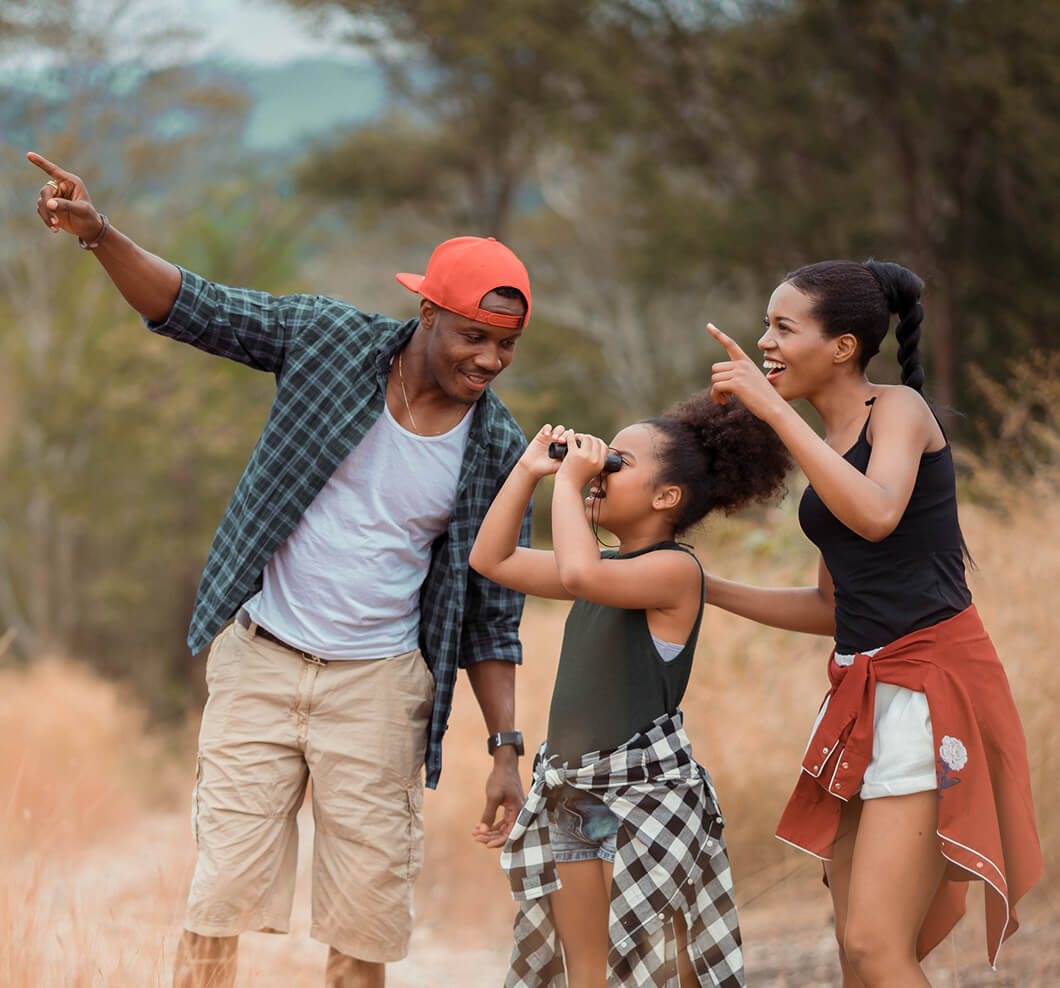 Parents pointing at something offscreen to their child who is using binoculars