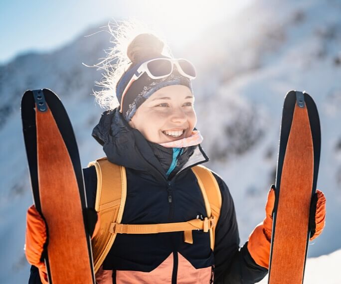 A skiier holding their skis smiling on a snowy mountain.